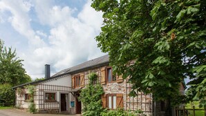 A stone house with a traditional half-timbered facade, a chimney, and a paved driveway. - Heritage Holiday Home in Roumont (Bertogne)