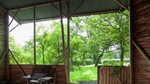 A covered outdoor area with a grill cart, wooden walls, and a view of a green landscape. - Heritage Holiday Home in Roumont (Bertogne)