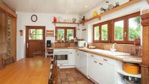 A kitchen with a wooden table, white cabinets, a stove, and a window. - Heritage Holiday Home in Roumont (Bertogne)