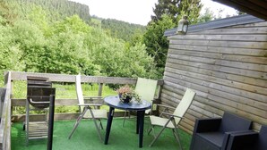 A patio with a round table, two chairs, a small table with a bowl, and a wooden fence.