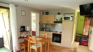 A compact kitchen with wooden cabinets, a microwave, and a stove. There is a dining table with chairs and a small window.