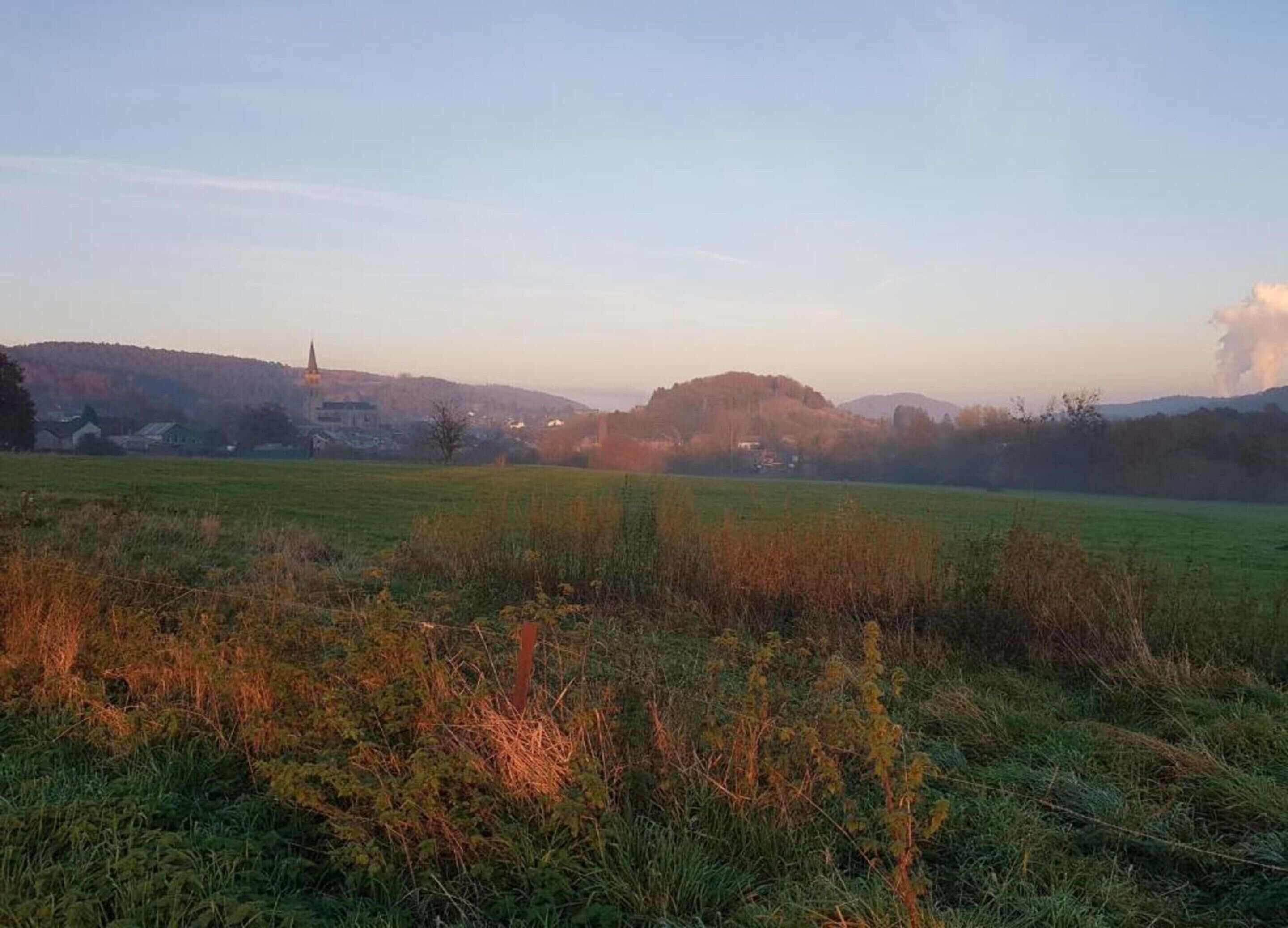 Un paysage rural avec une église, des champs ouverts et des collines en arrière-plan.