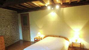 Quarto com cama de madeira, duas luminárias de cabeceira, cômoda de madeira e parede de pedra.