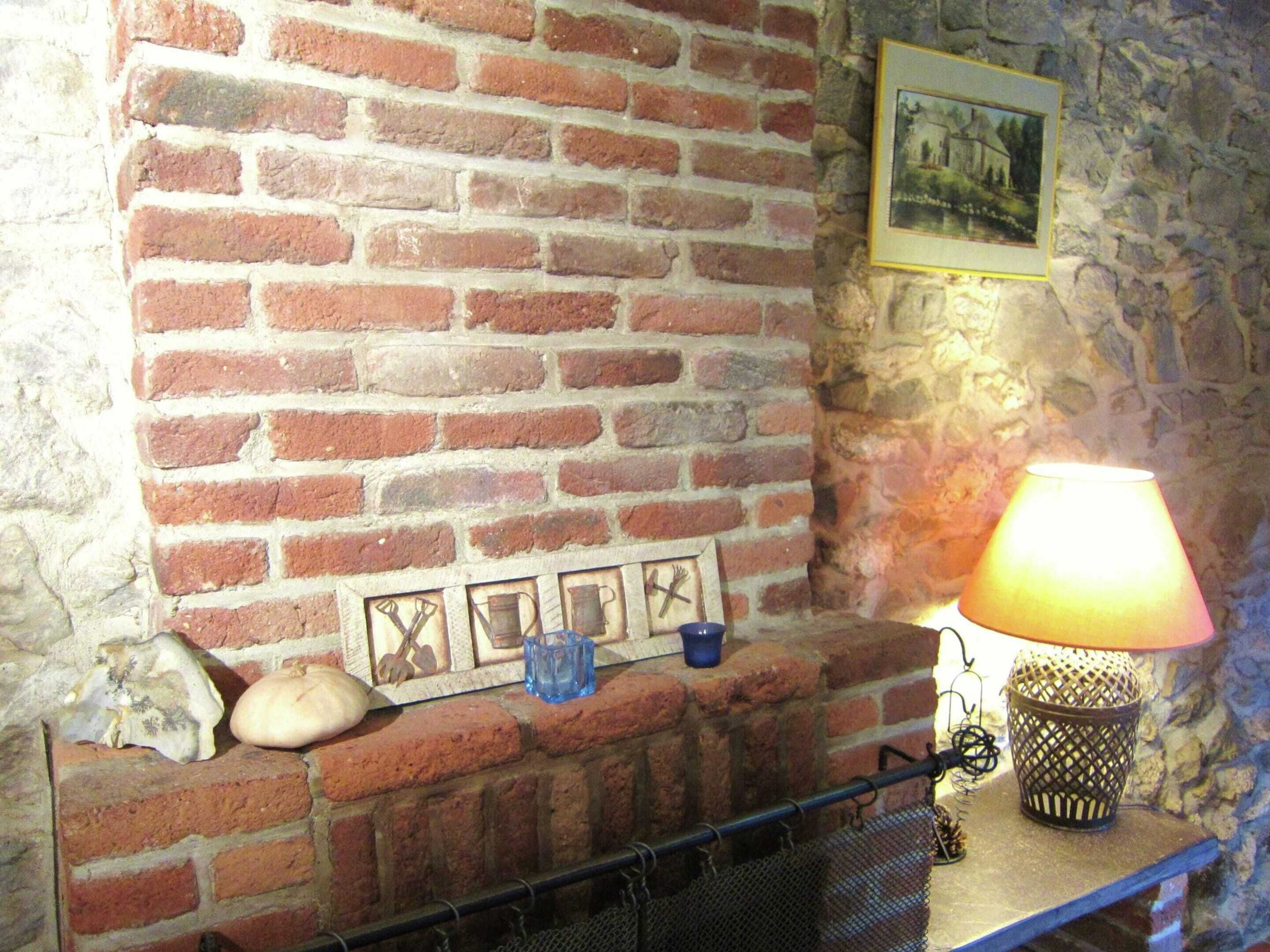 A brick fireplace with a metal screen, a framed picture above it, and a table lamp to the right.