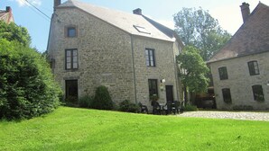 Um edifício de pedra com telhado inclinado, entrada com calçada e um gramado.