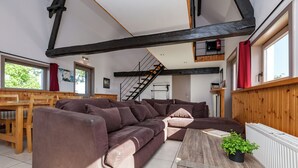 A modern living room with a large sectional sofa, wooden beams on the ceiling, a staircase, and a dining area with wooden furniture. - Spacious Countryside Farm Stay (Vleteren)