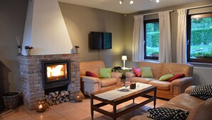 Un salon chaleureux avec une cheminée en briques, un canapé en cuir, une table basse en bois et un téléviseur fixé au mur.