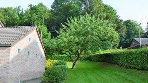 Un bâtiment en briques surmonté d’un toit en tuiles, entouré d’une pelouse bien entretenue et d’un grand arbre.
