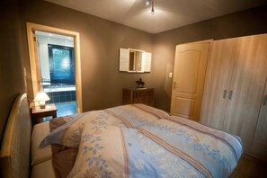 A bedroom with a bed, a nightstand with a lamp, a dresser, a mirror, and a wardrobe. - Modern Holiday Home in Stavelot With Fireplace (Stavelot)