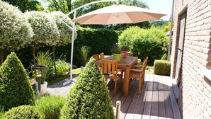 Une terrasse en bois avec une table et des chaises, entourée de verdure et d’un mur de briques.
