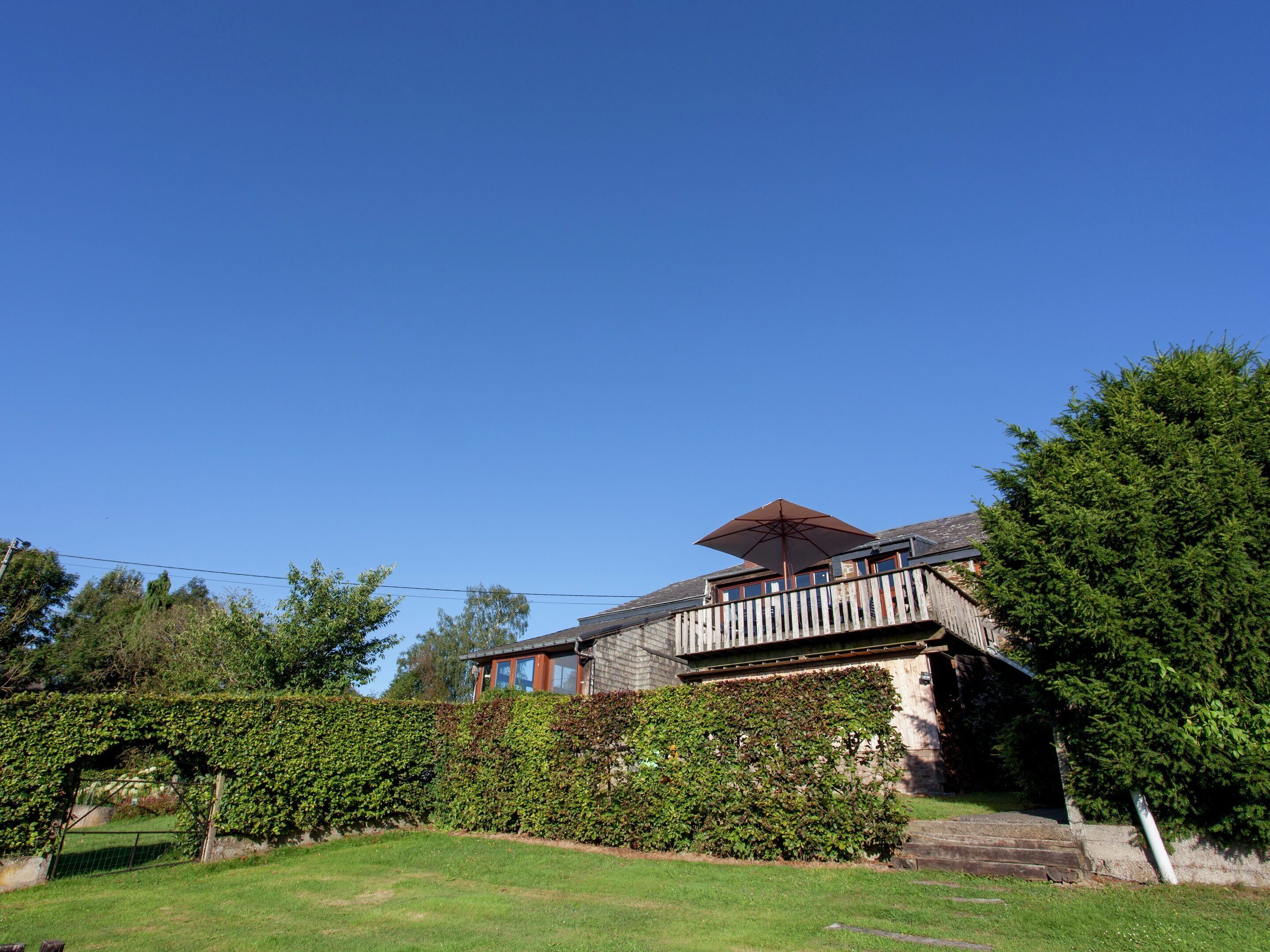 Een huis met een houten balkon, een grote parasol en een verzorgde tuin.
