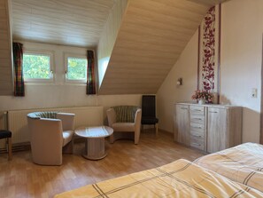 A room with a sloped ceiling, a bed, a sofa, a chair, a small table, a cabinet, and two windows with curtains. - Landhaus Nahe Sababurg Schloss (Trendelburg)