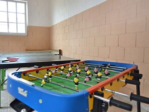 Ein Kicker und ein Pongtisch in einem Raum mit Backsteinwänden und einem Fenster.