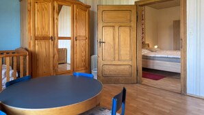 A room with a wooden wardrobe, a round table with chairs, and a bed in the adjacent room. - Landhaus Nahe Sababurg Schloss (Trendelburg)