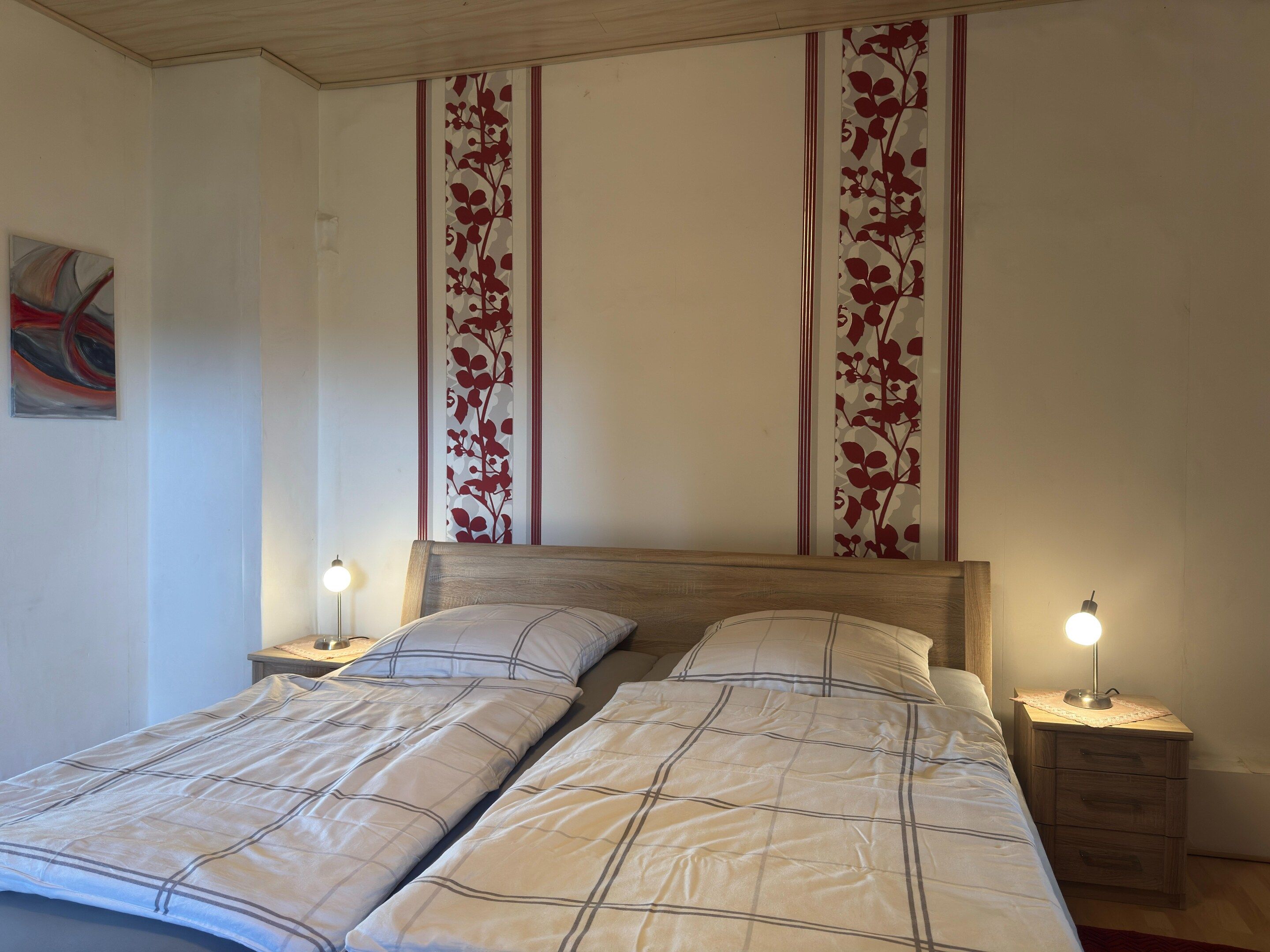 A double bed with a headboard, two bedside tables with lamps, and a wall with vertical floral patterns.