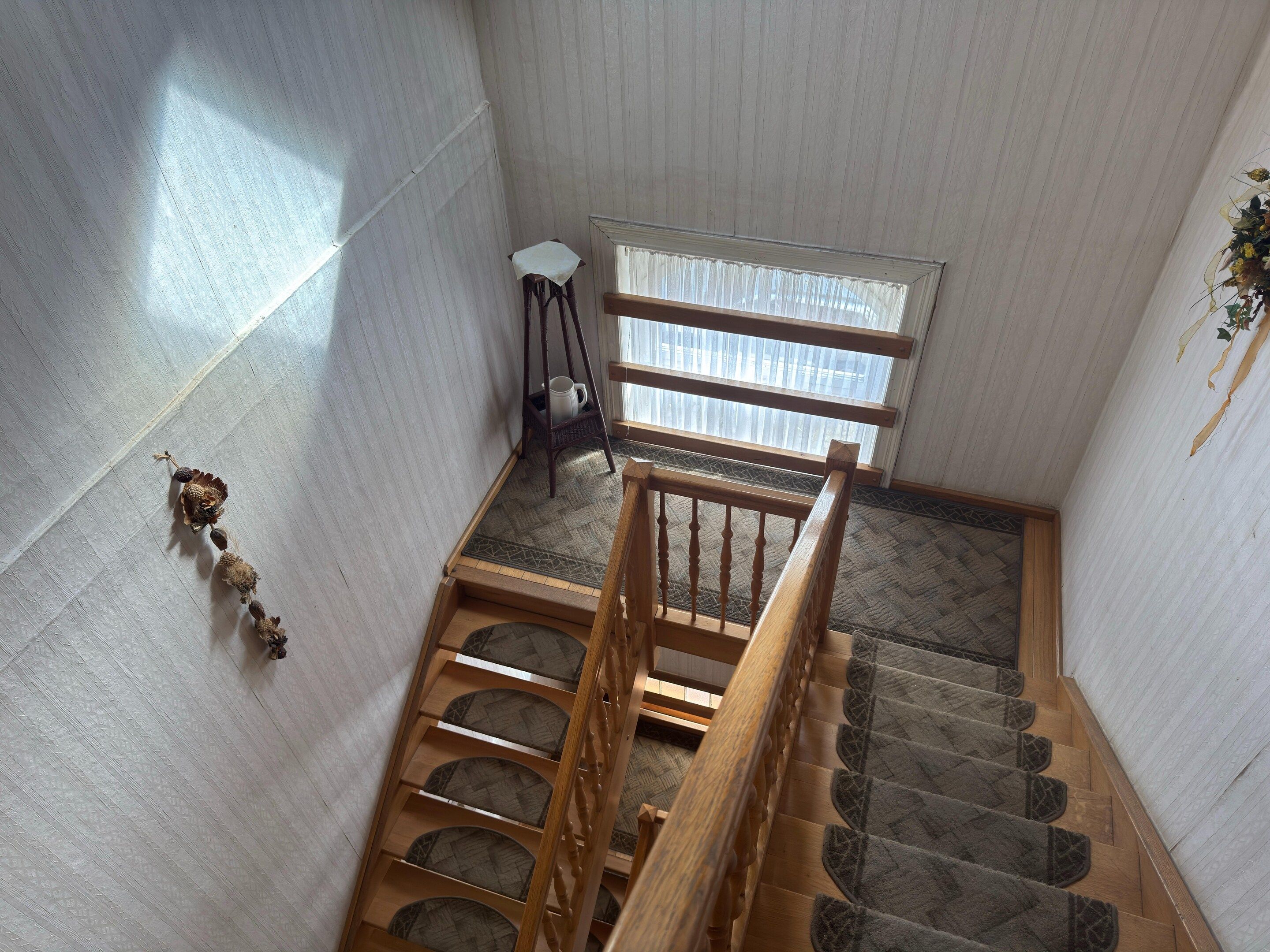 Un escalier en bois avec une rampe, menant à un palier doté d’une fenêtre.