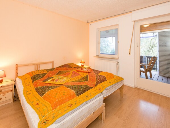 Une chambre à coucher avec un lit en bois, une table de chevet, une fenêtre et une vue sur la terrasse extérieure.