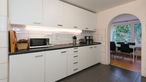 Uma cozinha moderna com armários brancos, micro-ondas e máquina de café. É possível ver uma área de refeições com mesa e cadeiras através de um arco.