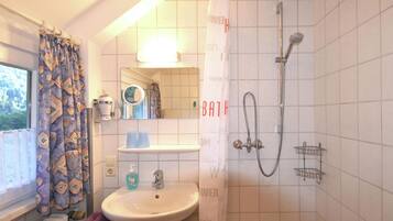 Ein Badezimmer mit Waschbecken, Spiegel, Dusche und einem Fenster mit Vorhängen.