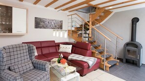 A living room with a red sofa, a plaid armchair, a glass coffee table, a wooden staircase, and a wood-burning stove. - Comfortable Holiday Home in Saxony With Terrace (Oederan)
