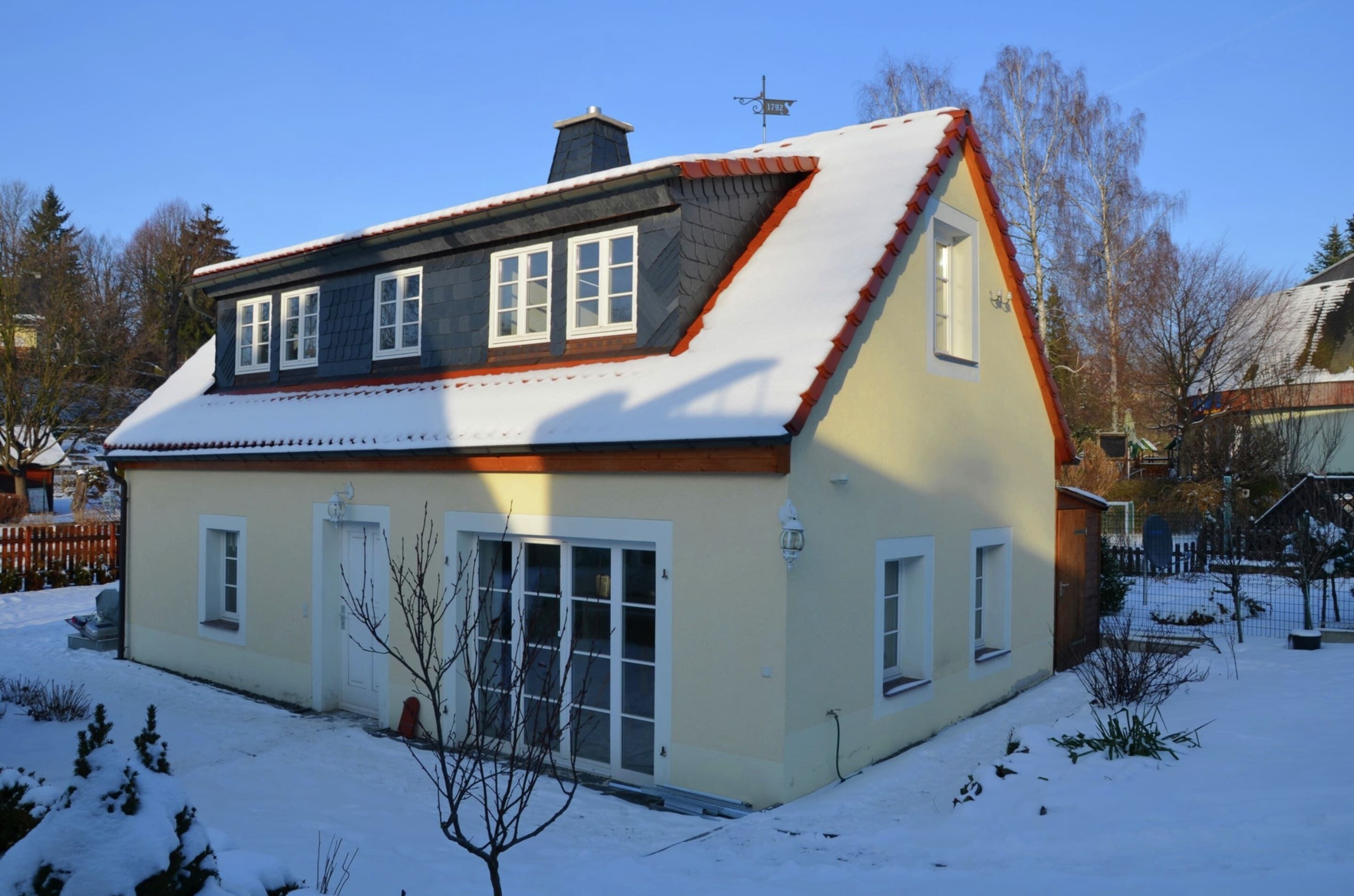 Ett tvåvåningshus med ett sluttande tak, en skorsten och en snötäckt trädgård.