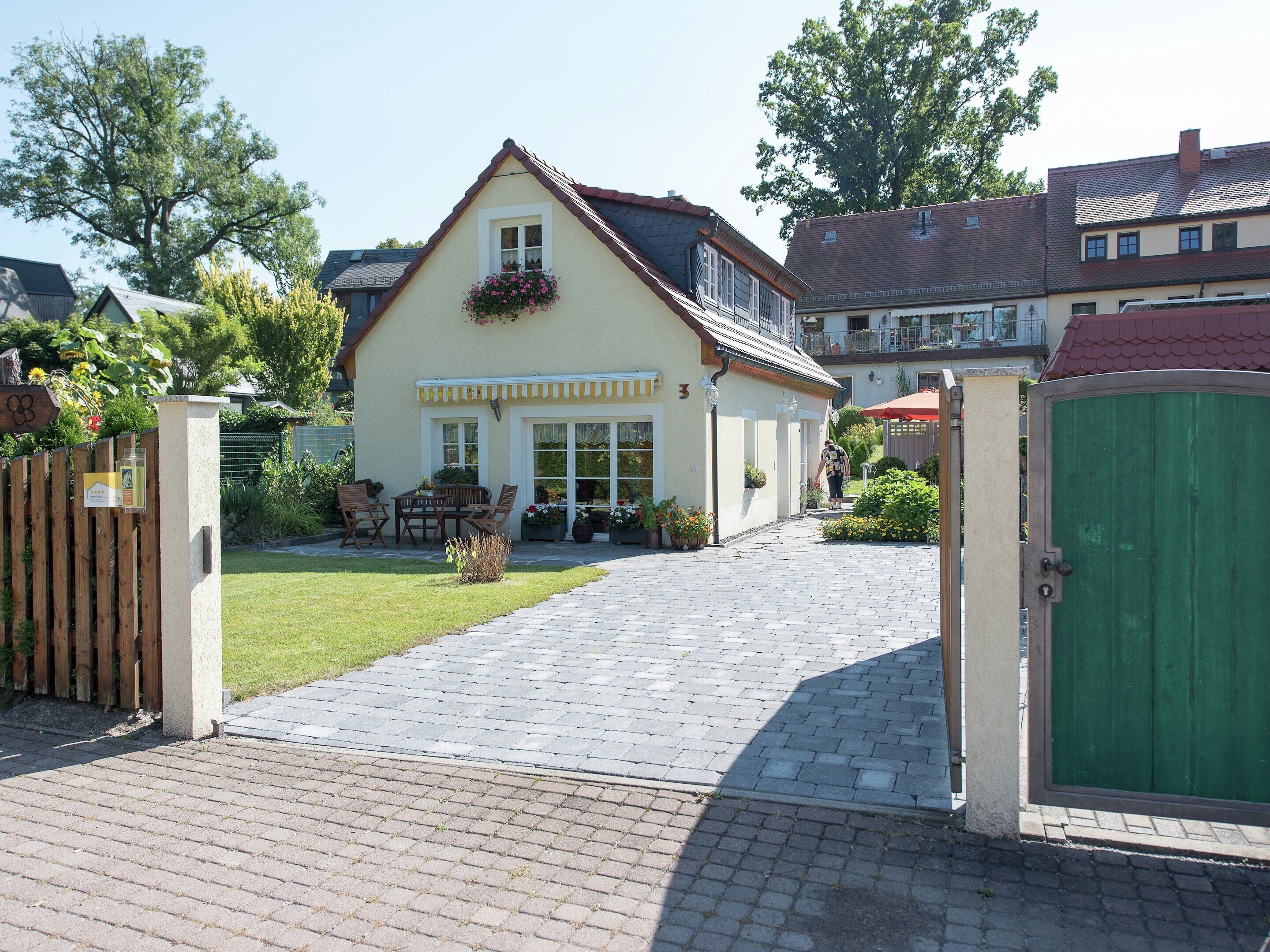 A two-story house with a paved driveway leading to a gated entrance.