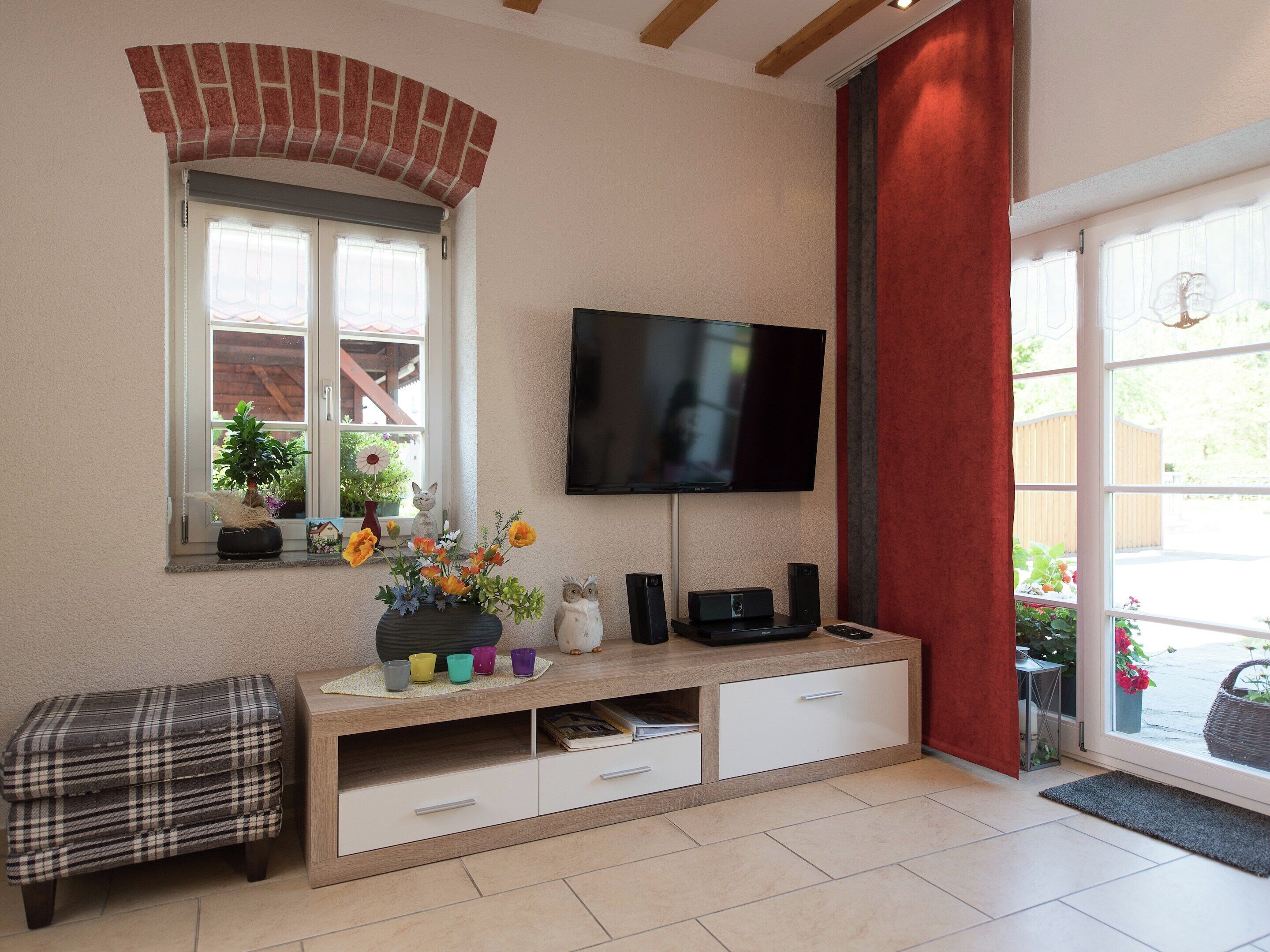 Sala de estar con televisión, ventana con plantas, banca y cortina roja.