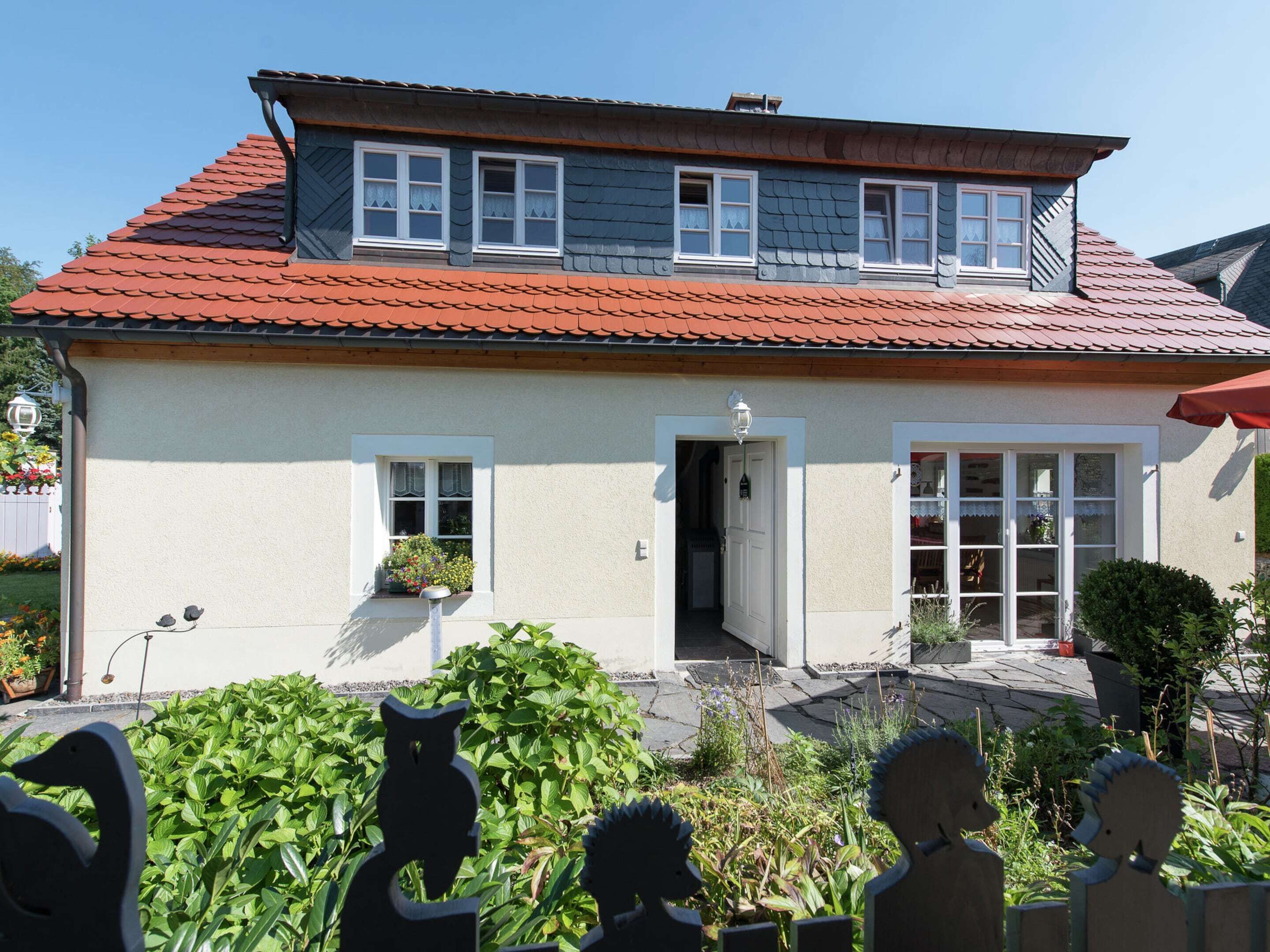 A two-story house with a red-tiled roof, white exterior walls, and a front door with a small porch area.