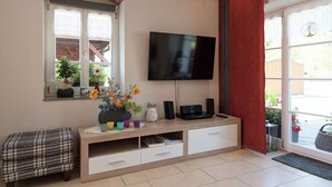 A living room with a TV, a window with plants, a bench, and a red curtain. - Comfortable Holiday Home in Saxony With Terrace (Oederan)