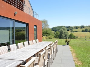 An outdoor dining area with a long wooden table and chairs, large windows, and a view of rolling hills. - Superb Holiday Home With Barbecue (Plombieres)