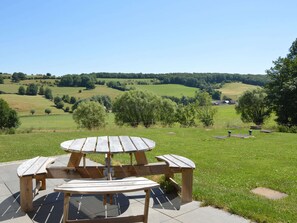 Une table de pique-nique avec des bancs, installée dans un espace verdoyant, offrant une vue sur des collines ondulantes et des arbres.