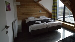 A bedroom with a sloped ceiling, wooden walls, a bed with white linens, a window with curtains, and a sign on the wall. - Superb Holiday Home With Barbecue (Plombieres)
