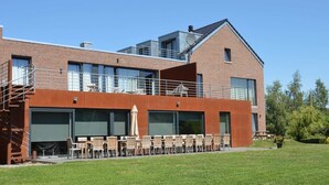 A modern building with a brick facade, large windows, and outdoor seating area with tables and chairs. - Superb Holiday Home With Barbecue (Plombieres)