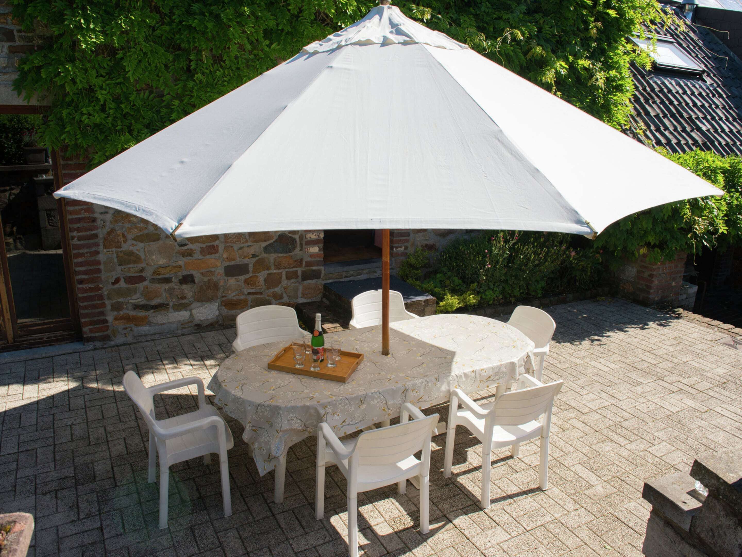 A round table with six white chairs and a large white umbrella.