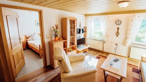 A cozy room with a wooden ceiling, a bed, a sofa, a small table, a bookshelf, and a window with curtains. - Modish Apartment in Plankenstein near Forest (Plankenfels)