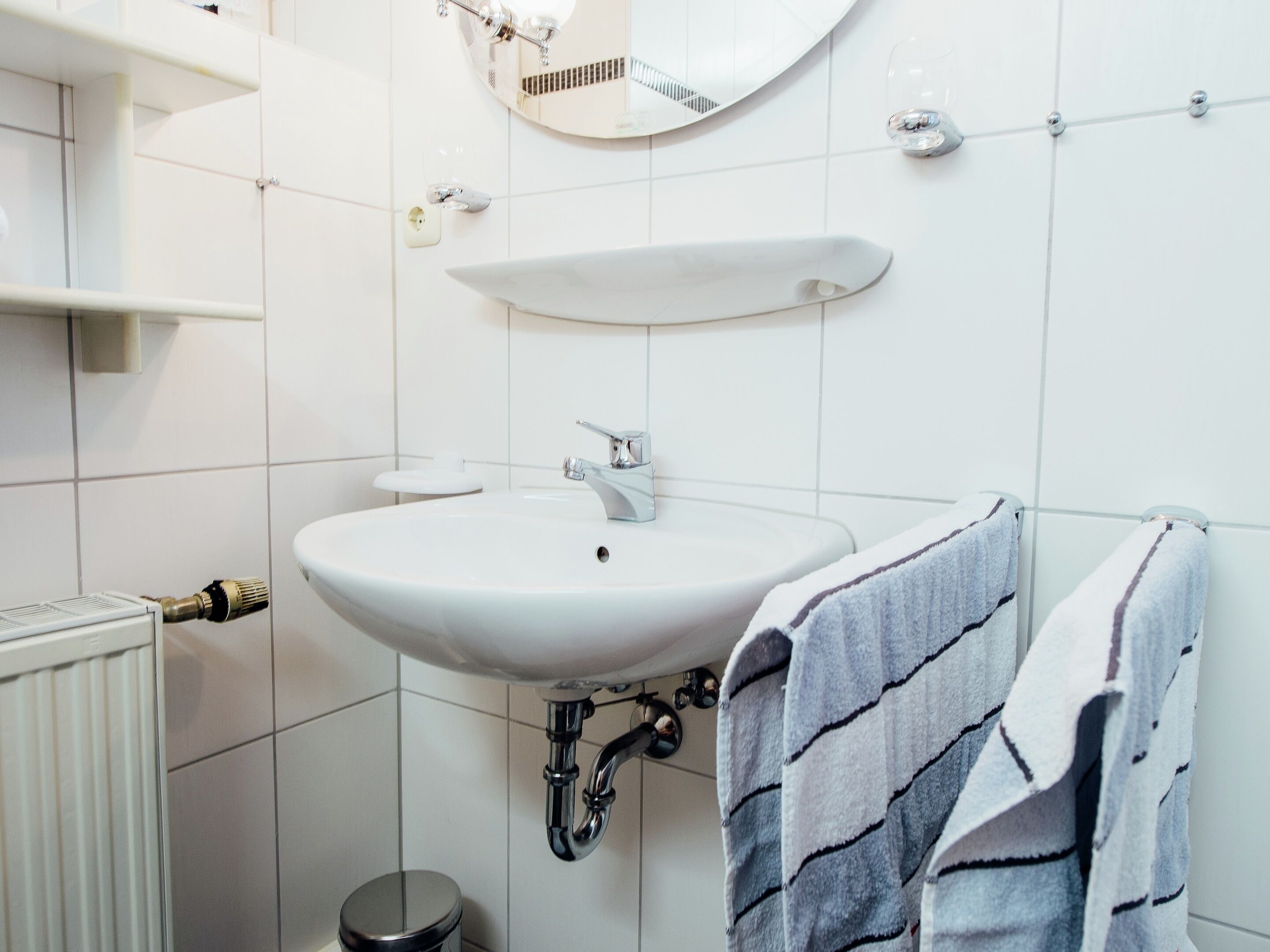 Un baño con un lavamanos blanco, un espejo y una toalla colgada en la pared.