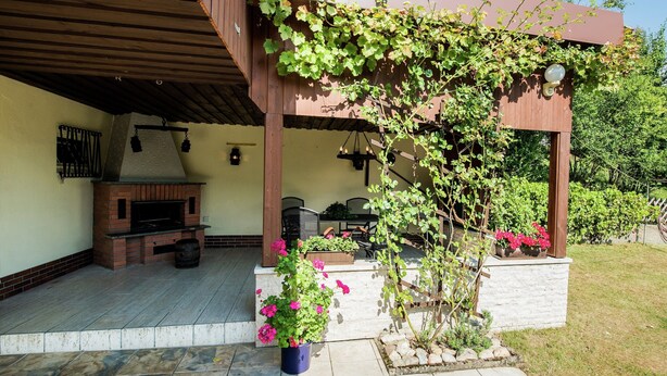 A covered outdoor patio with a brick fireplace, outdoor furniture, and potted plants. - Modish Apartment in Plankenstein near Forest (Plankenfels)