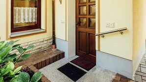 A house entrance with a wooden door, a window with a curtain, a brick step, and a metal handrail. - Modish Apartment in Plankenstein near Forest (Plankenfels)