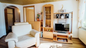 A living room with a white sofa, wooden cabinets, a TV, and a bookshelf. - Modish Apartment in Plankenstein near Forest (Plankenfels)