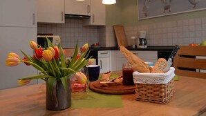 A kitchen with white cabinets, a wooden table, a vase of tulips, a basket of bread, and a painting of birds on the wall. - Ferienwohnung mit Sauna (Nieheim)
