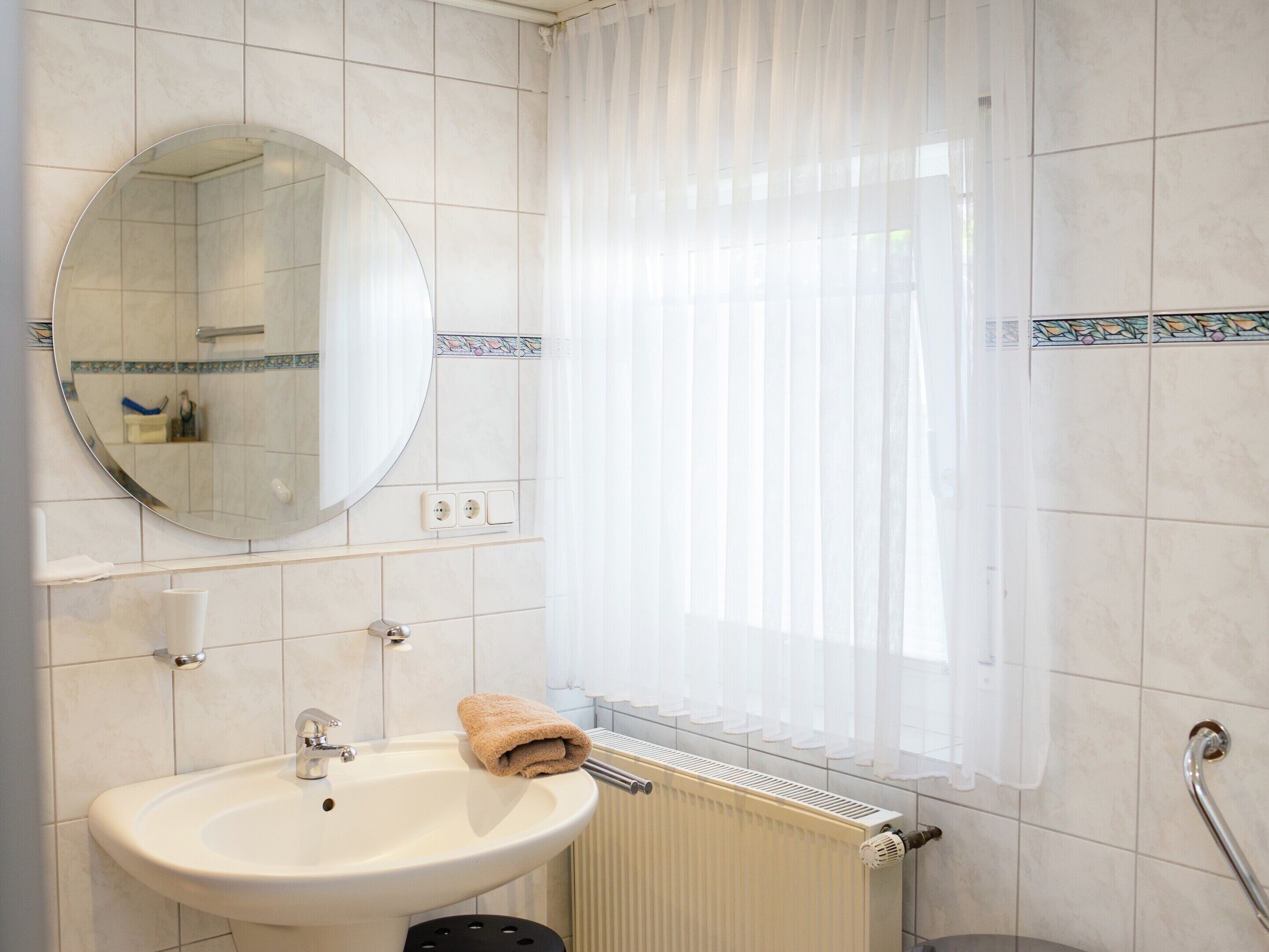 A bathroom with a sink, mirror, towel, and window with sheer curtains.