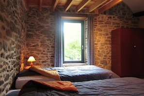 A stone-walled room with a bed, a window with curtains, and a wooden wardrobe.