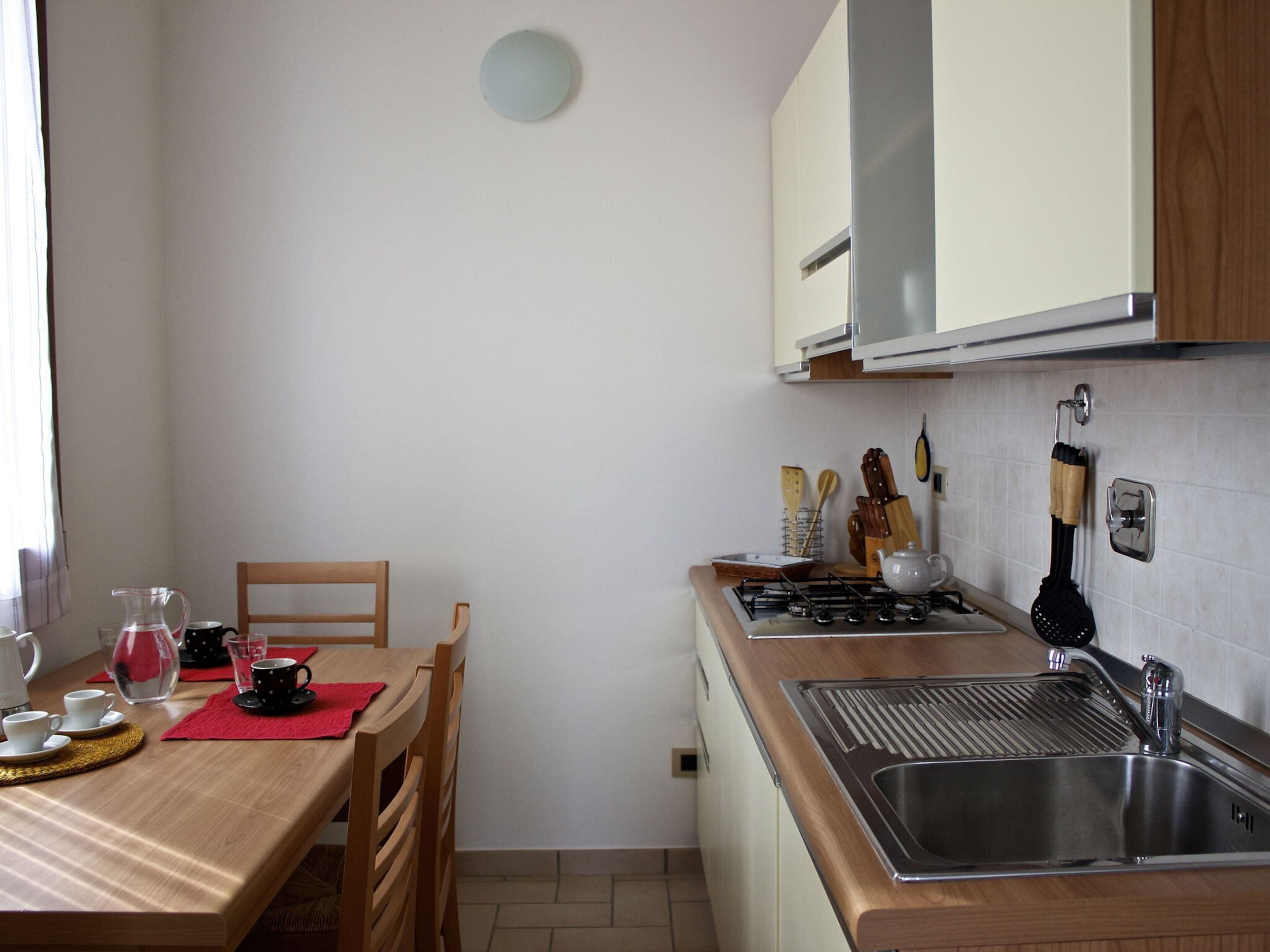 A compact kitchen with a wooden table and chairs, a gas stove, a sink, and basic kitchen utensils.
