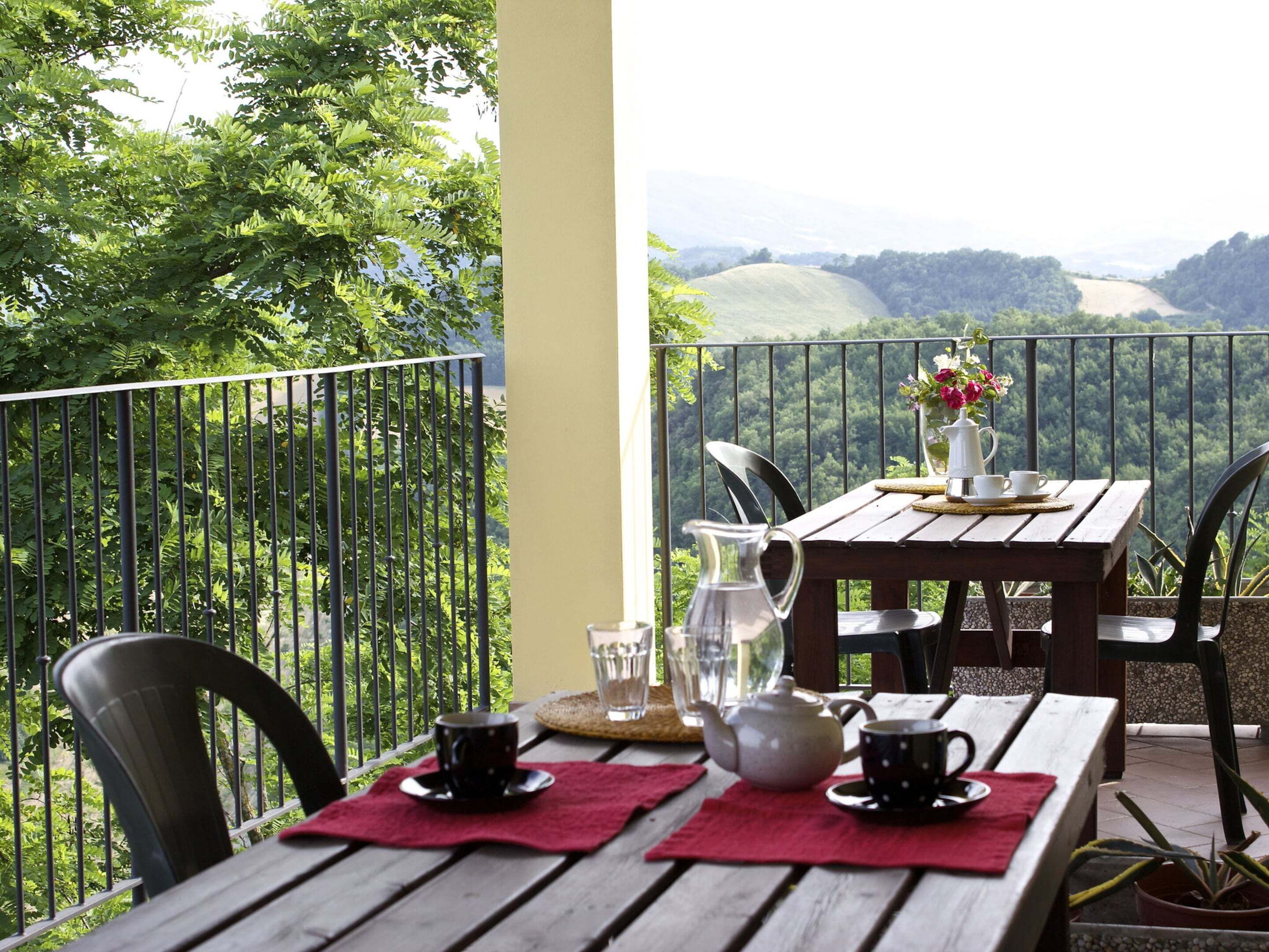 A wooden table with two cups and a teapot on a balcony with a view of green hills.
