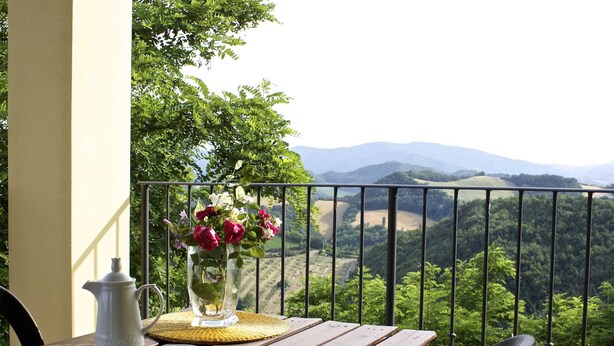 A wooden table with a white teapot, two cups, and a vase of flowers on a balcony overlooking a mountainous landscape. - Stay With Balcony Views (Casalfiumanese)