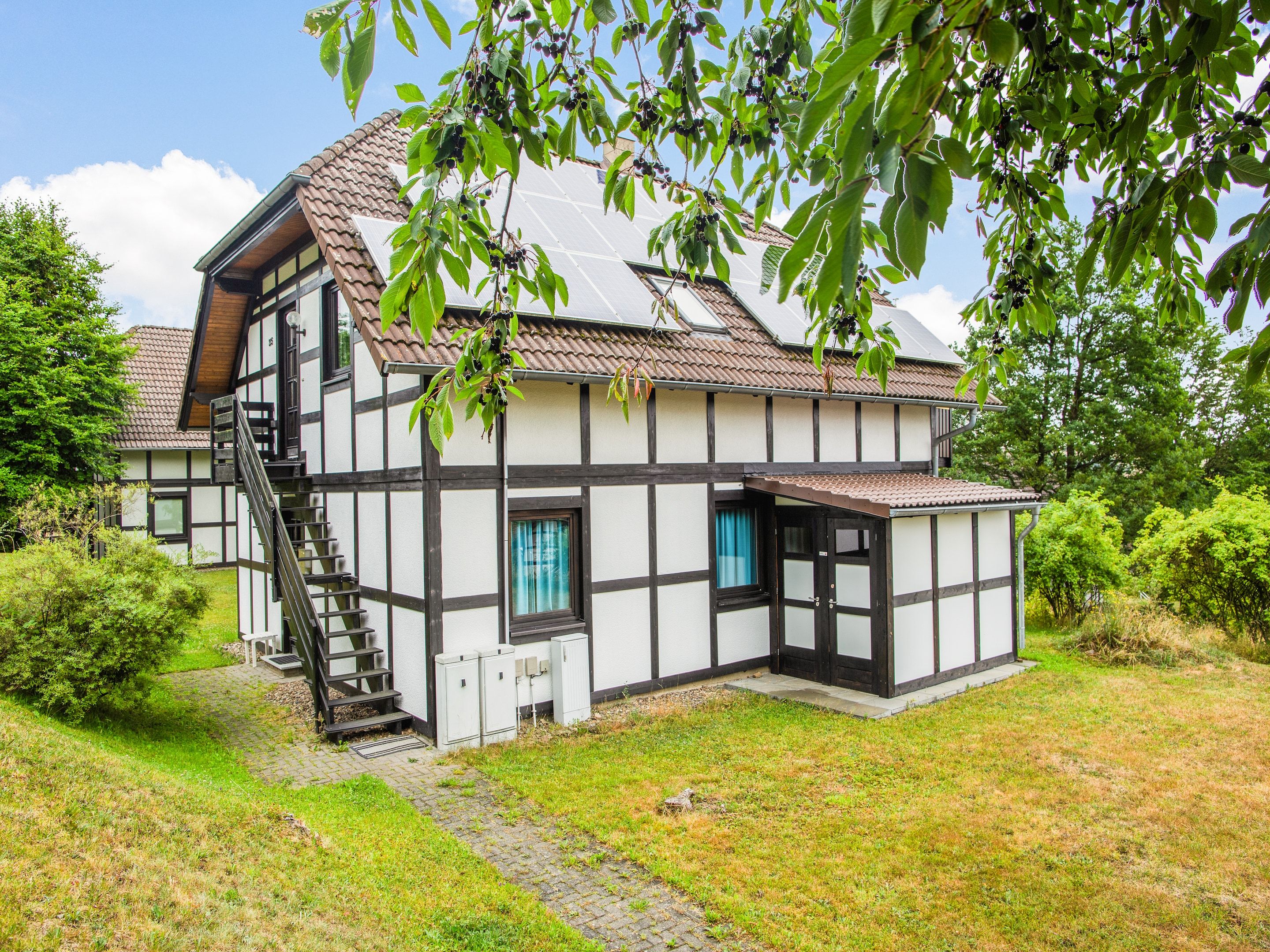 A traditional half-timbered house with a visible staircase leading to the entrance, surrounded by greenery.