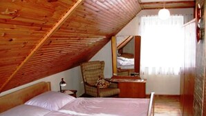 Un dormitorio con techo inclinado, cama, silla, mesita de noche y espejo.