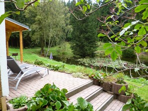 A patio with a wooden pergola, a table, and chairs. There is a pond with lily pads and a birdhouse. - Holiday Home in Thuringia Near Rennsteig (Friedrichroda)