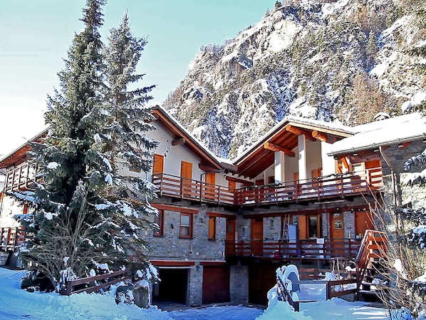 Un chalet doté d’un balcon en bois, de murs en pierre et surplombant une montagne enneigée.