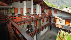 A traditional chalet with a wooden balcony, stone walls, and a mountainous backdrop.